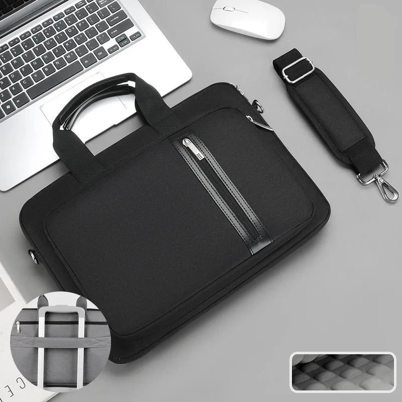 Black laptop bag with handle and shoulder strap on a gray surface with a laptop and mouse.