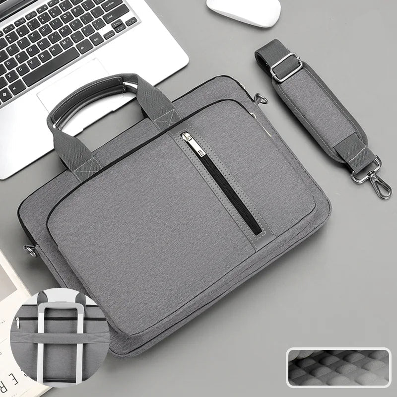 Grey laptop bag with handle and shoulder strap on a grey surface with a laptop.