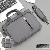 Grey laptop bag with handle and shoulder strap on a grey surface with a laptop.